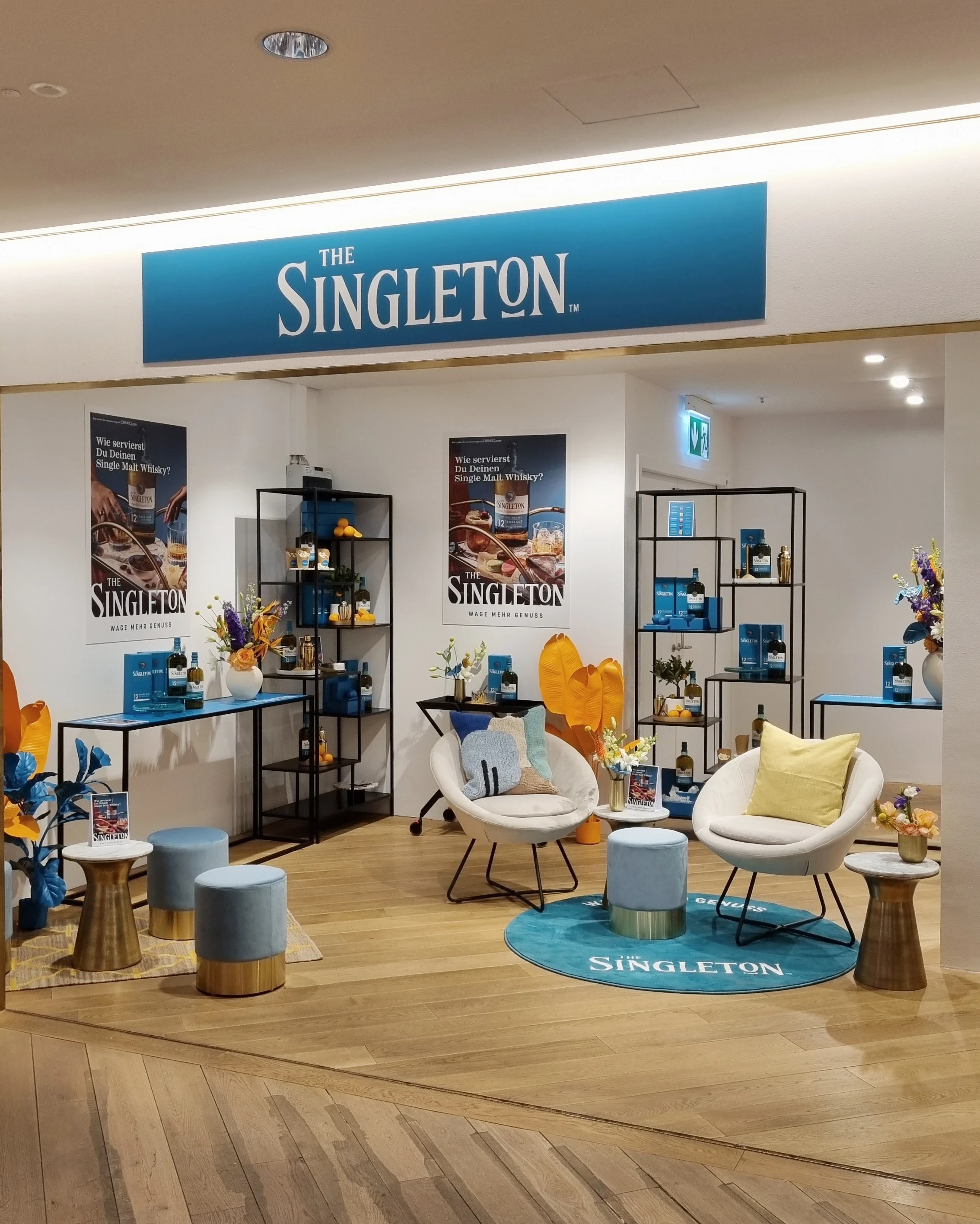 Singleton lounge area with white armchairs, blue poufs, posters and large logo banner.