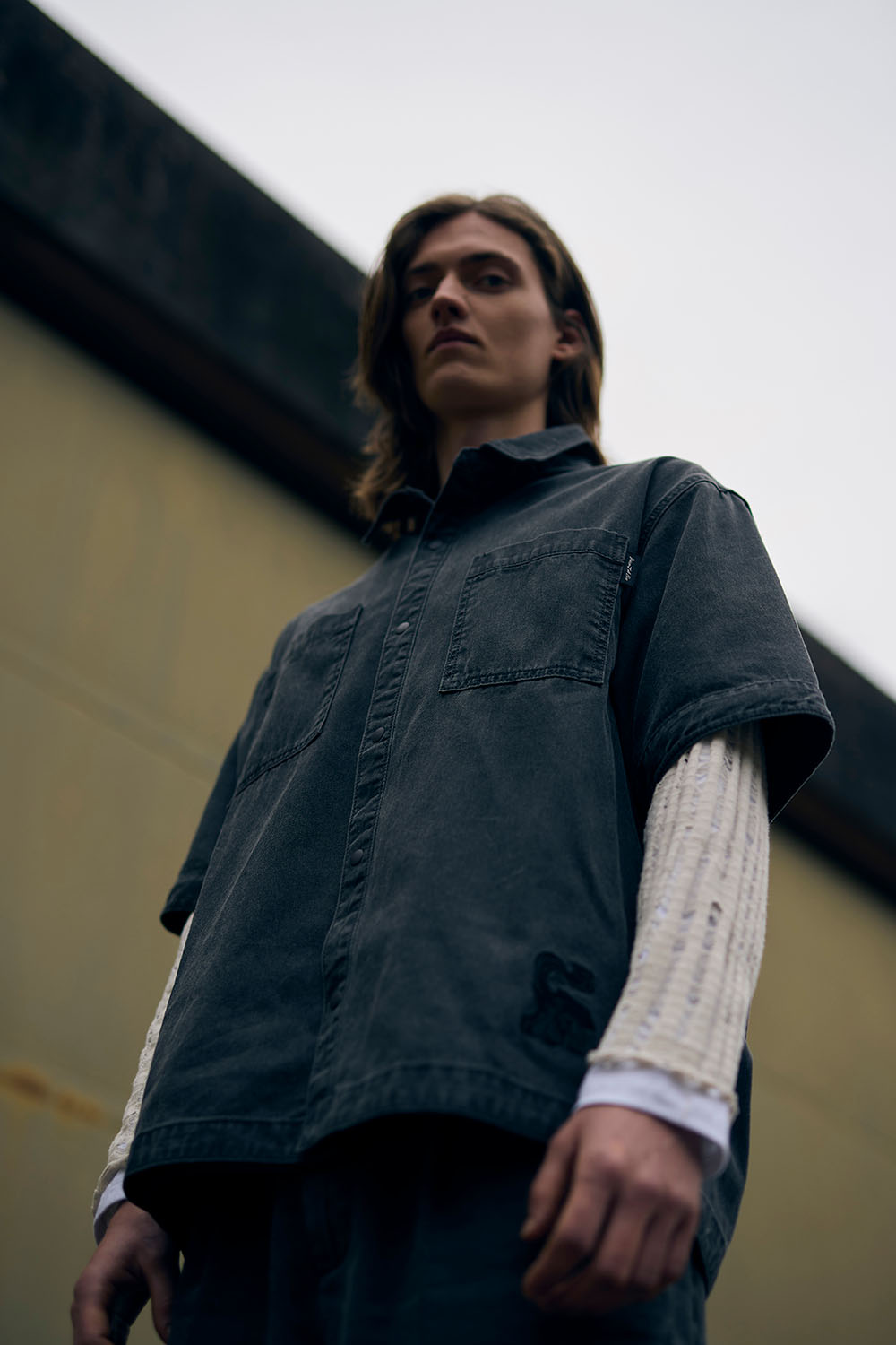 Low-angle portrait of a model wearing a dark layered look at the former military airbase.