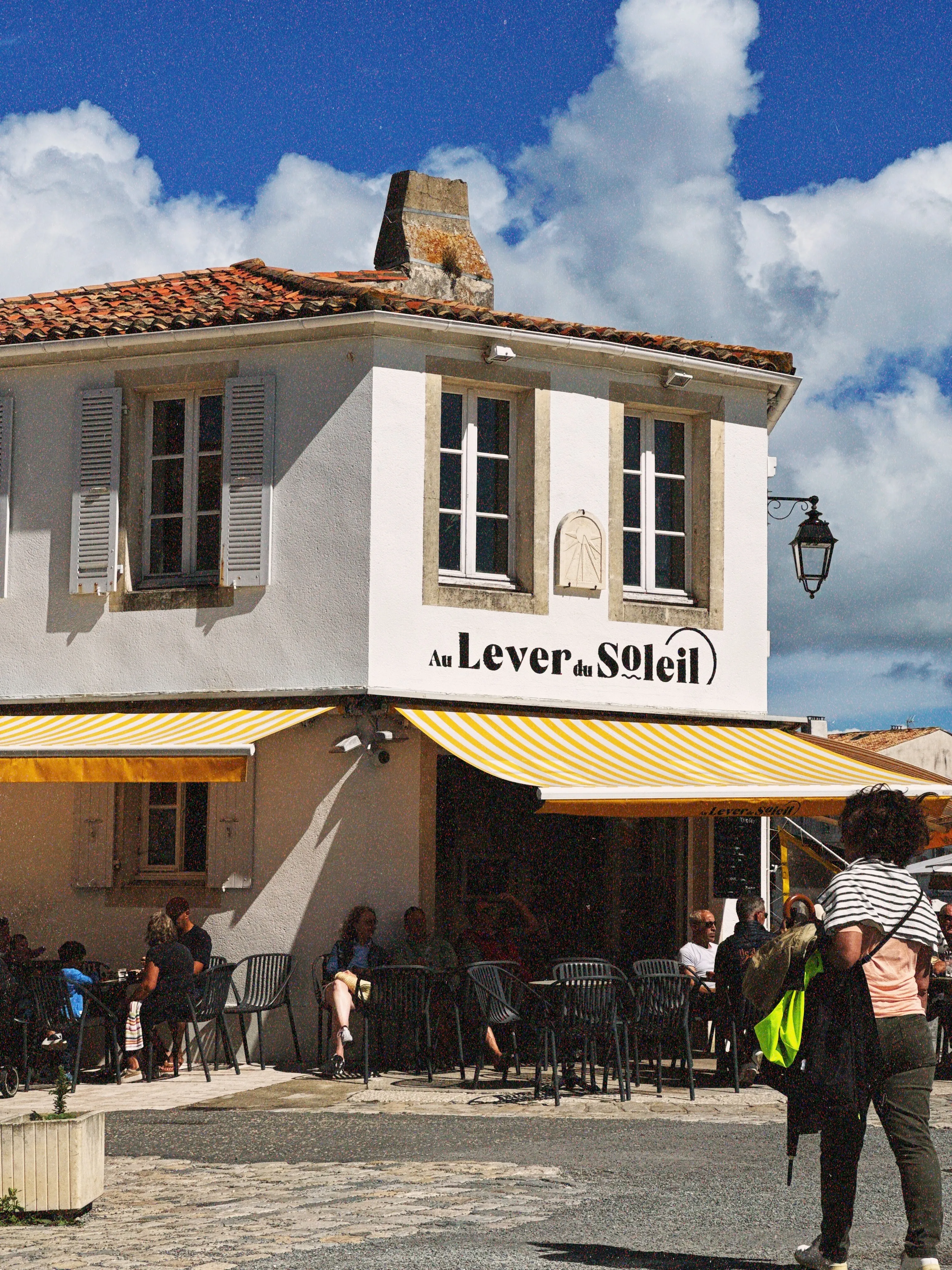 Petit café à Saint martin de ré, au soleil avec des passants devant la terrasse du café