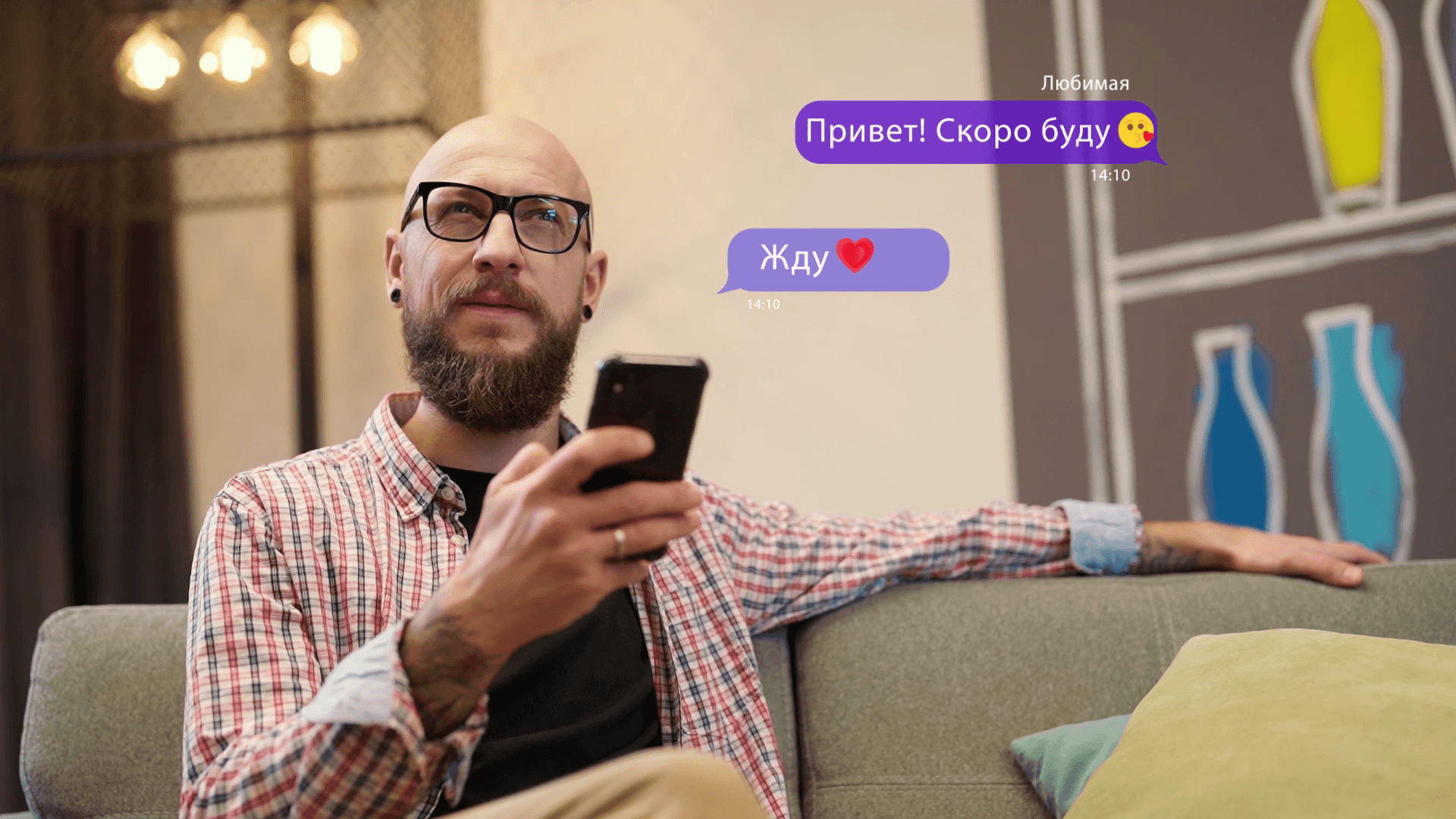 A man sits pensively on a sofa and looks at his phone.