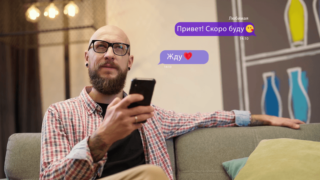 A man sits pensively on a sofa and looks at his phone.