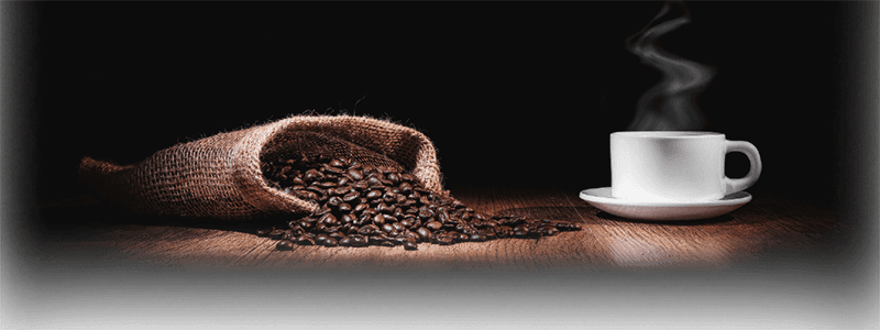 Coffee beans spilling from burlap sack with steaming white cup on dark background