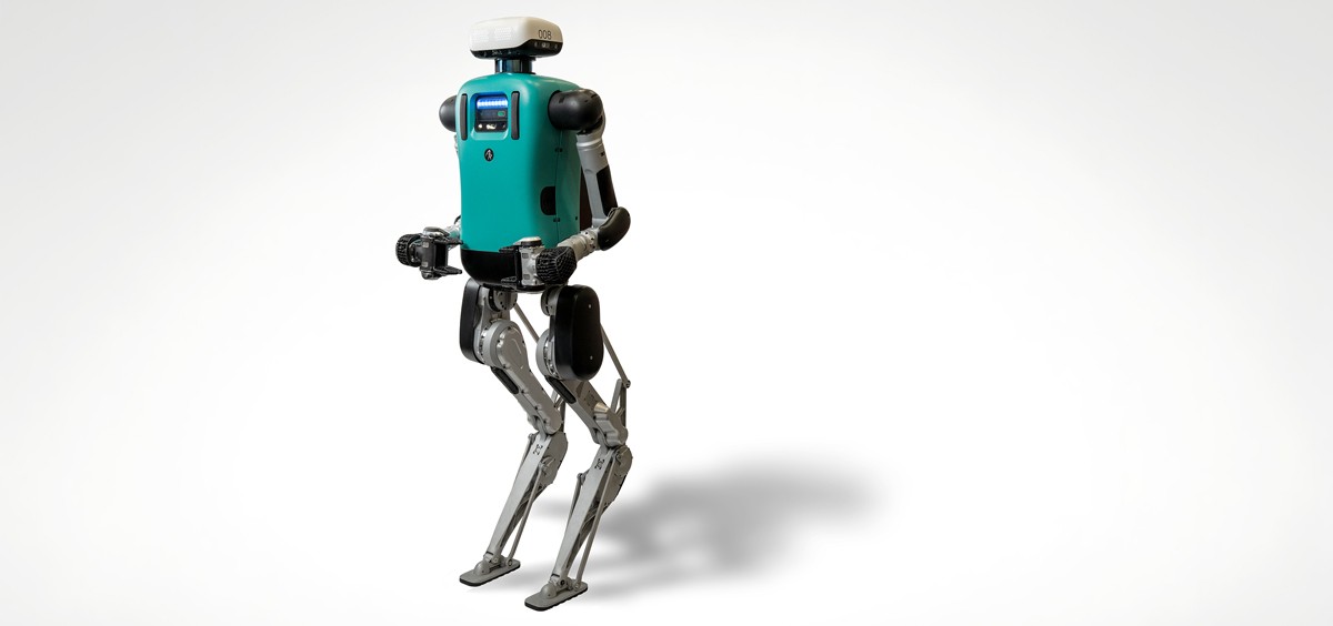 A humanoid robot with a teal torso, mechanical arms, and metal legs stands upright against a plain white background, illustrating a modern robotic coworker.