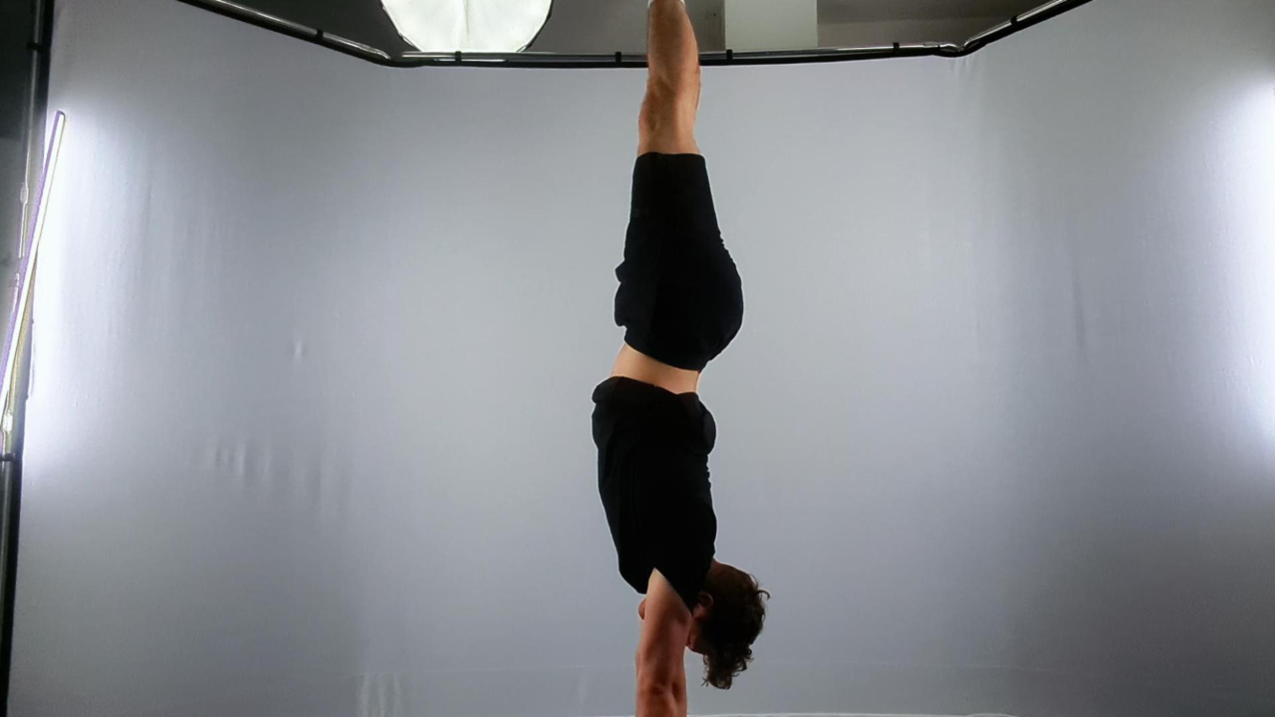 A person performs a perfect handstand in a professional photography studio with soft lighting, showcasing balance and strength.