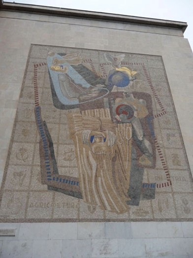 A stone mosaic on a building façade in Rome depicting different human figures.
