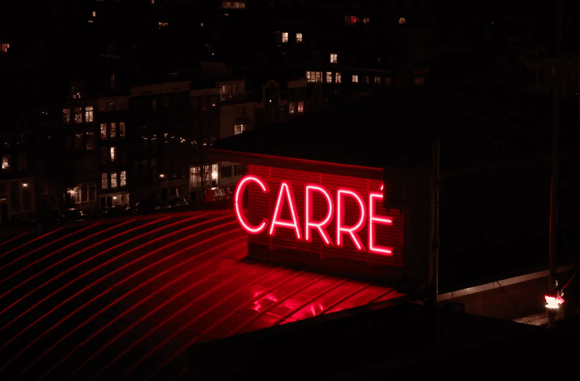 A glowing red sign displays the word "CARRE" against a dark background, with blurred lights in the distance.