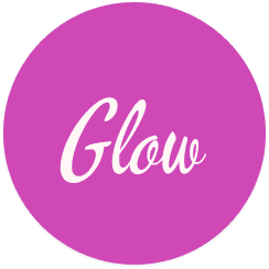 Young person with wavy hair poses confidently in sunlight against a modern building backdrop. Wears a black blazer and silver necklace, conveying elegance.