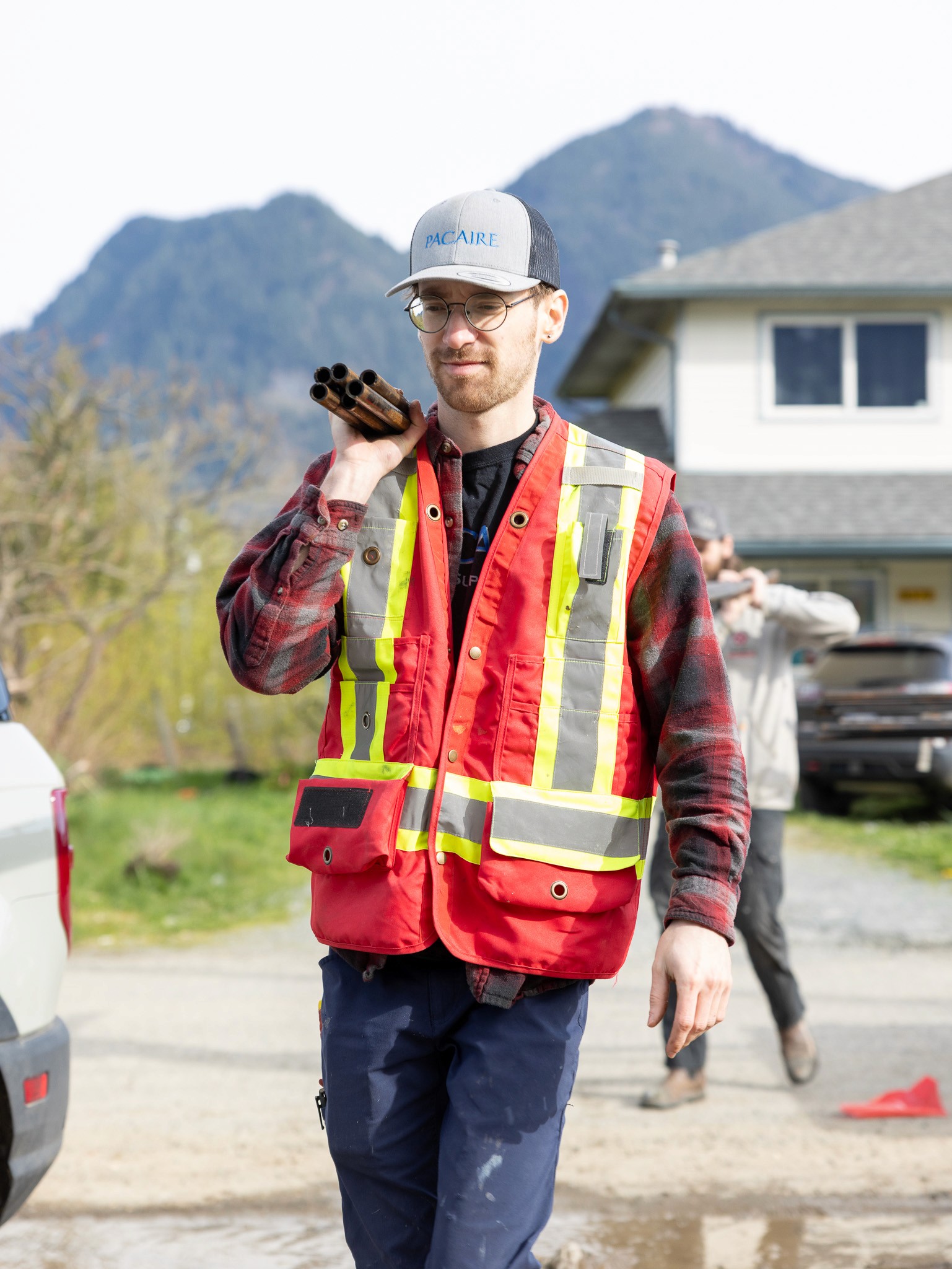 Man in safety vest carrying pipes in Agassiz, Fraser Valley, British Columbia for plumbing and HVAC.