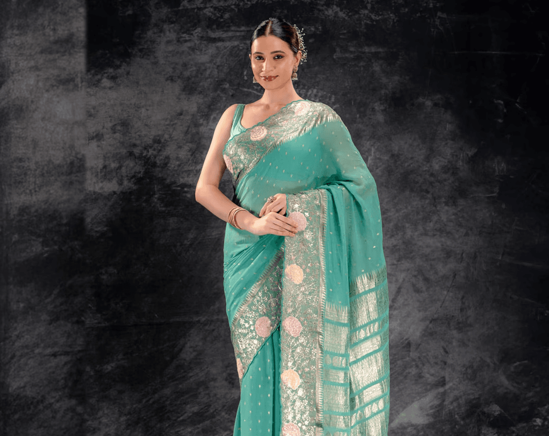 A woman wearing a teal blue georgette saree with shimmering golden borders from That Saree Shop, showcasing the saree’s lightweight flow and graceful, festive elegance.