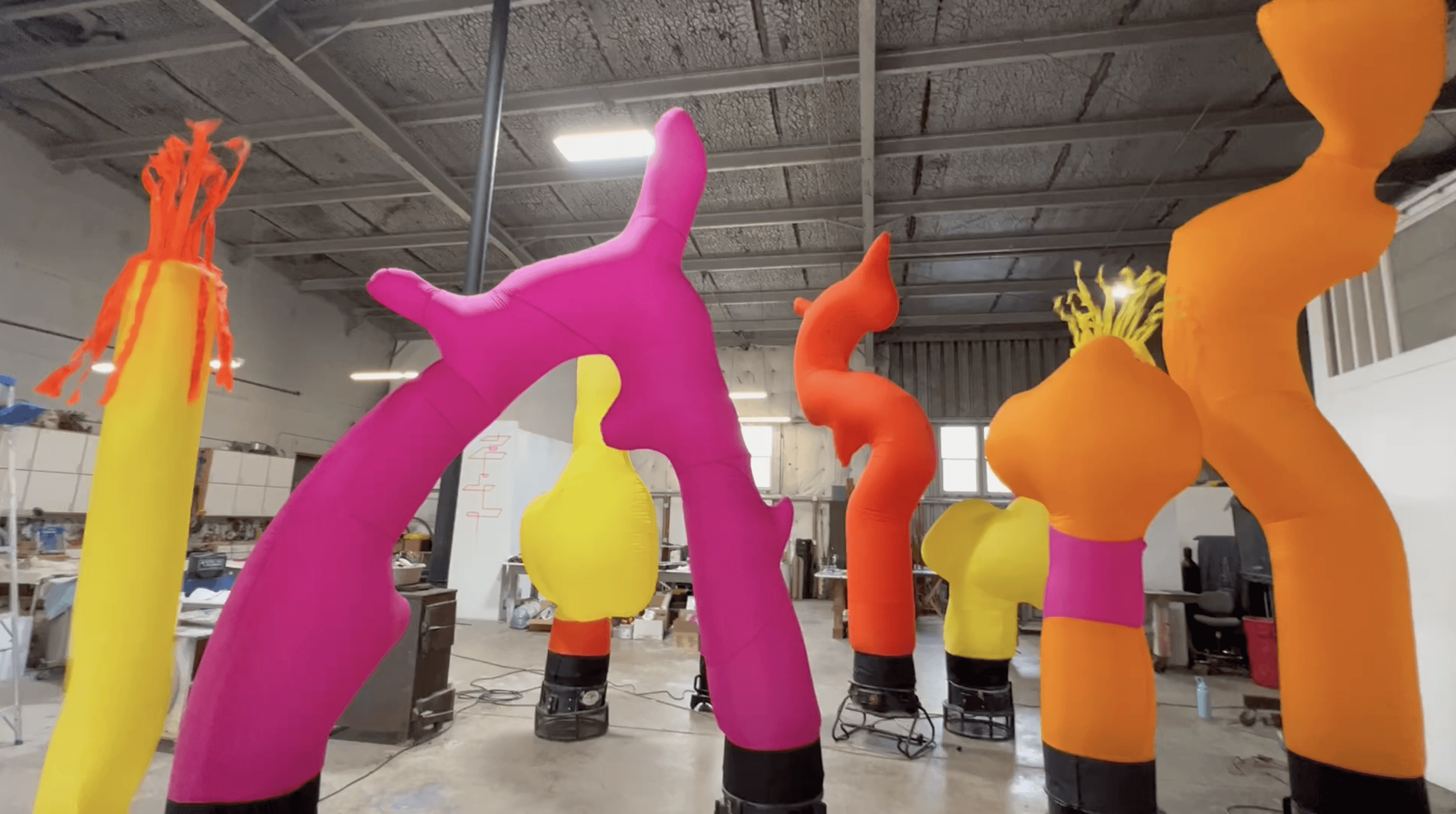 Colorful inflatable figures in vibrant pink, yellow, and orange are displayed indoors, creating a whimsical atmosphere.