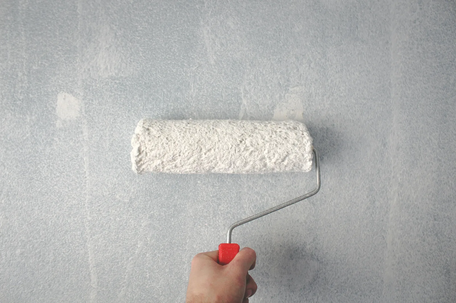 Hand holding white paint roller against light grey wall