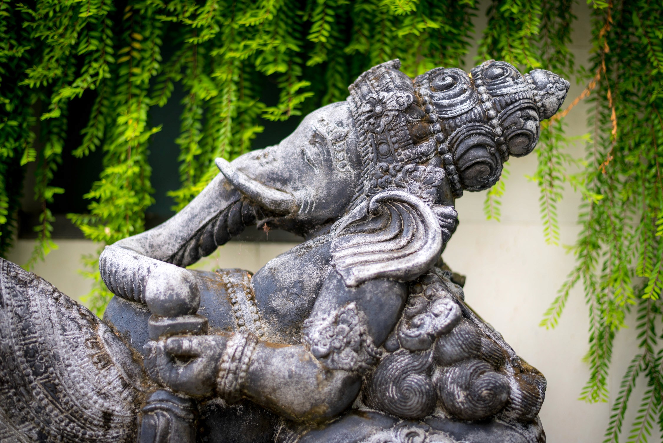 A stone sculpture of a mythical creature with a dragon-like head and scales sits against a backdrop of green foliage.