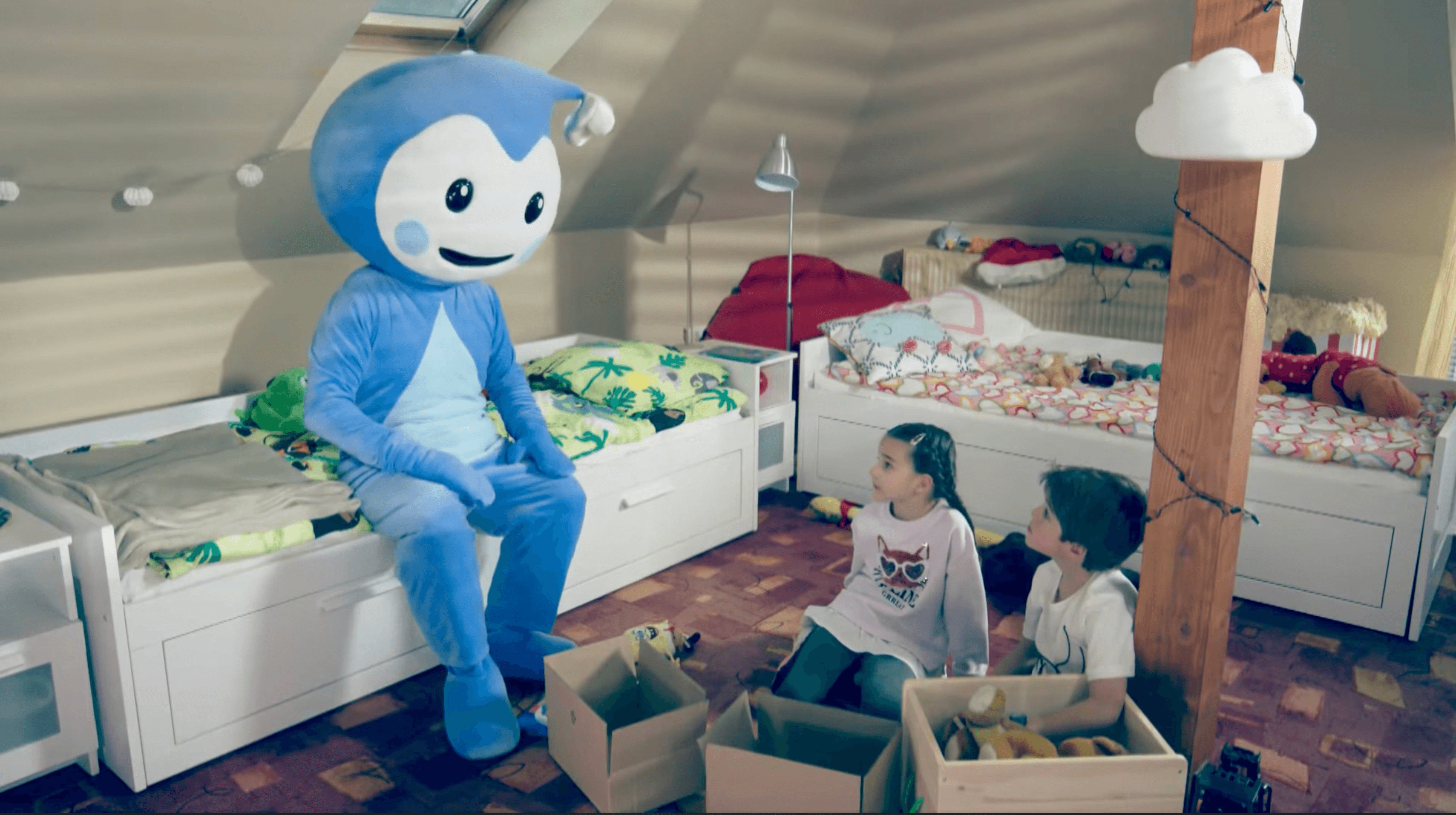 Cseppbarát kékl kabalafigurája beszélget a testvérpárral a szobájukban játékok között.