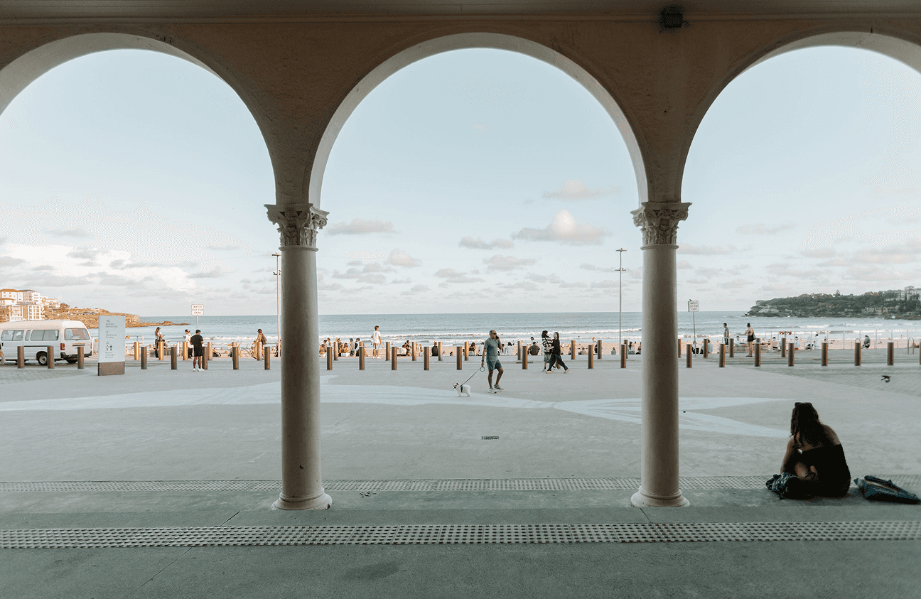 View of a lively beach and promenade framed by three arches.