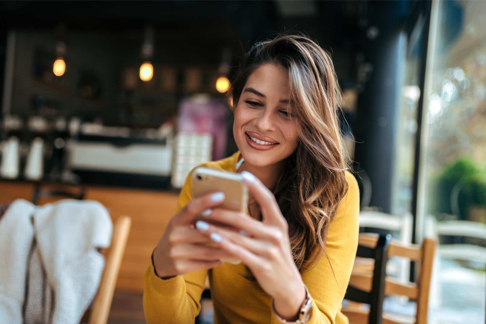 Beautiful young woman reading text message on mobile phone at the cafe