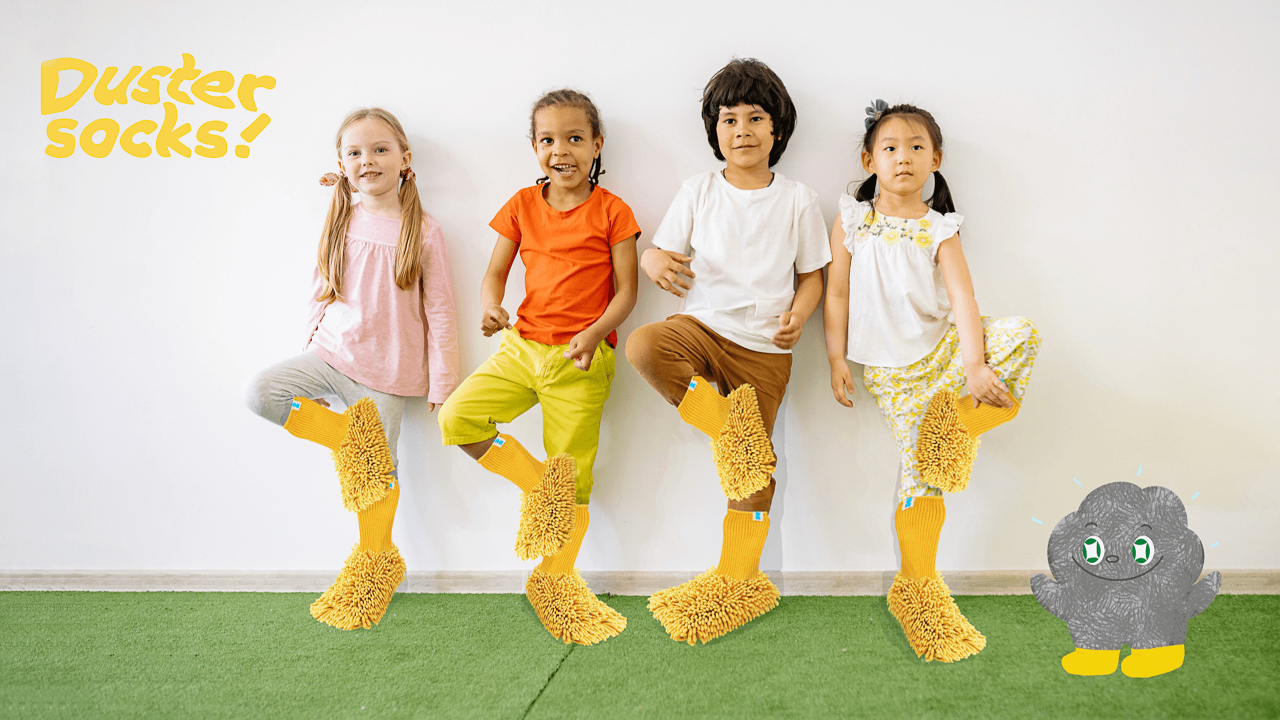 Four children stand against a white wall, each wearing yellow socks with fuzzy tops. The child on the far left wears a pink long-sleeved shirt and gray pants. The child next to them wears an orange short-sleeved shirt and yellow pants. The third child wears a white short-sleeved shirt and brown pants. The child on the far right wears a white short-sleeved shirt with a yellow floral pattern and light-colored pants. A gray cartoon character with green eyes sits on the green carpet near the wall. The words “Duster Socks!” appear in yellow letters in the top left corner.