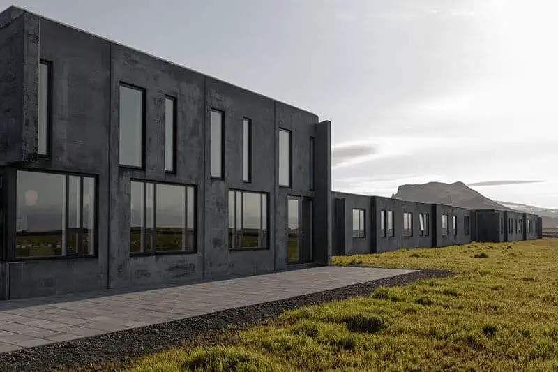 Long concrete hotel building alongside a green lawn and paved path, with a mountain in the distance