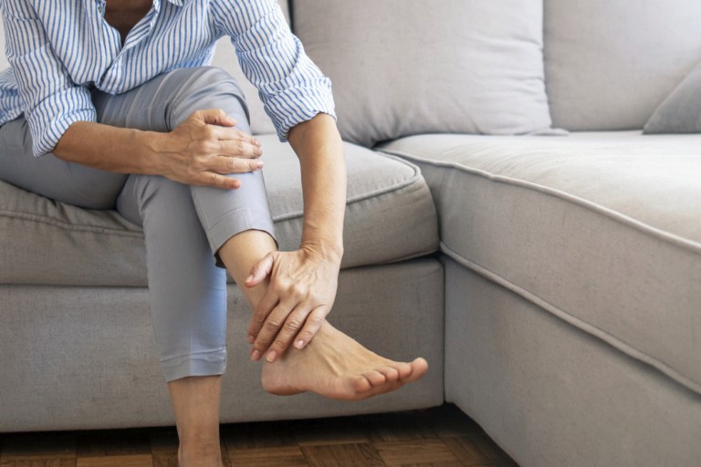 Person sitting on a sofa holding their ankle in pain.