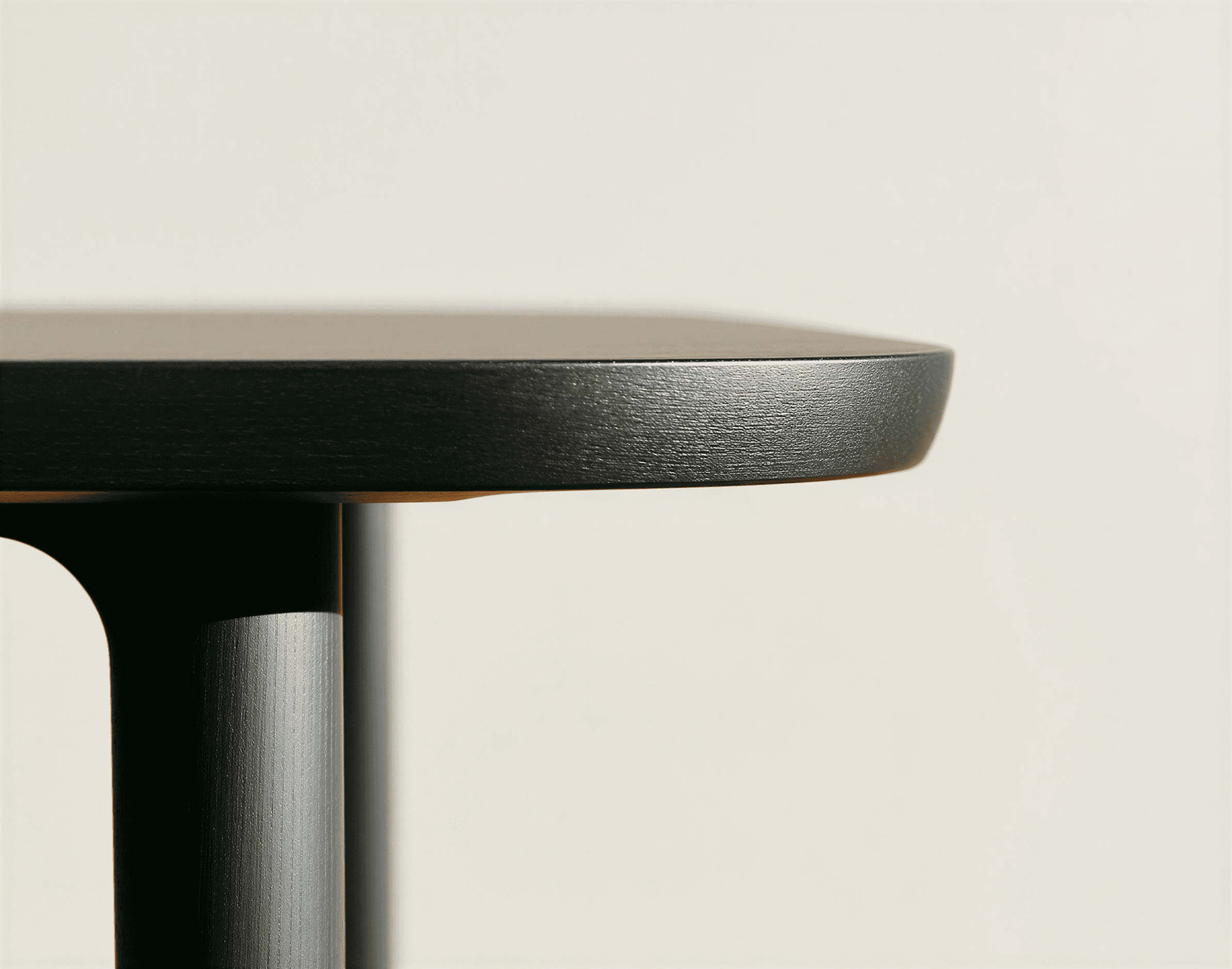 Close-up of a sleek, modern table with a dark, rounded edge and cylindrical leg, set against a neutral beige background.
