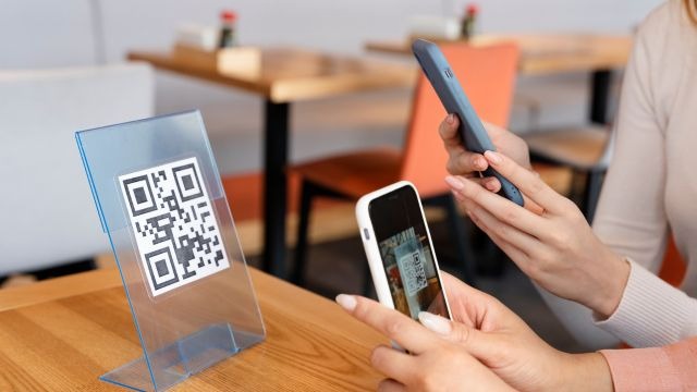 Mulheres apontando celulares para placa com QR code em ambiente de restaurante