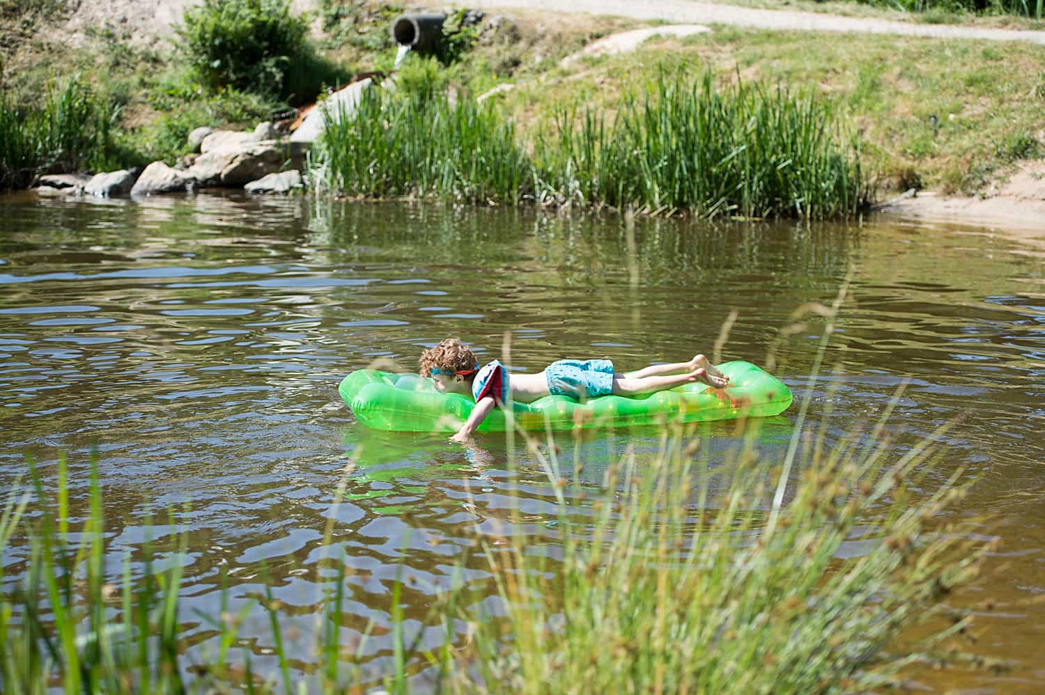 Kind mit grüner Luftmatratze auf dem Badesee