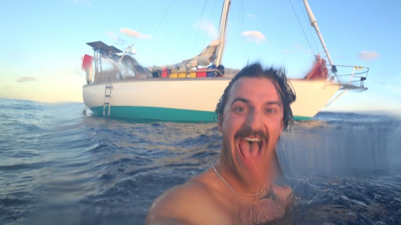 Xander swimming in the ocean with his early sailboat behind him