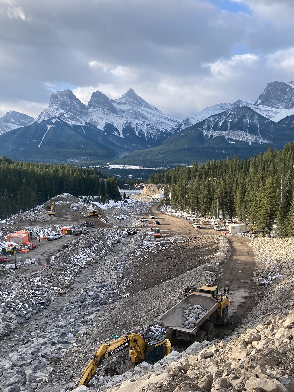 Steep construction access road and lock block retaining wall under construction at Cougar Creek Dam site near Canmore