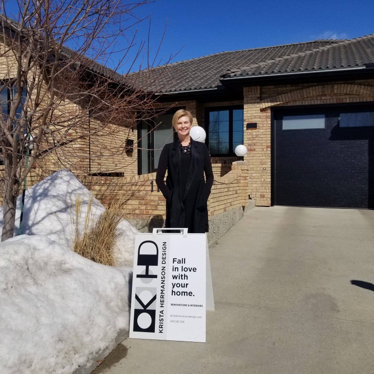 Image of KHD Homes signage in front of luxury home with woman standing beside it smiling.