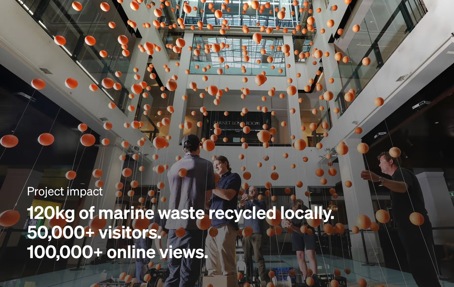 Photo looking up through the suspended orange spheres in the Customs House atrium, overlaid with project impact stats: 120kg of marine waste recycled locally, 50,000+ visitors, 100,000+ online views.