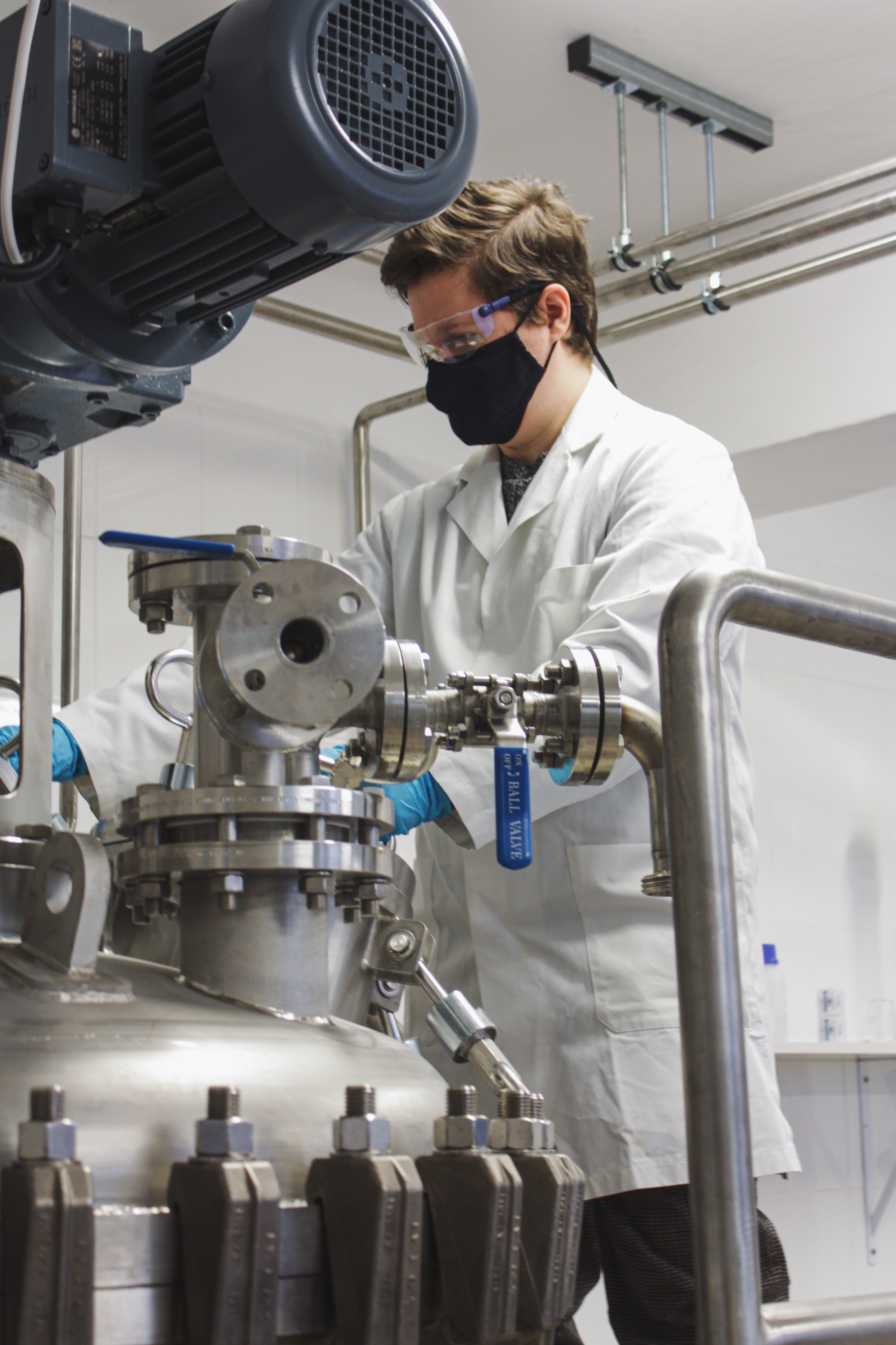 Scientist in lab coat, mask, and goggles working with equipment.
