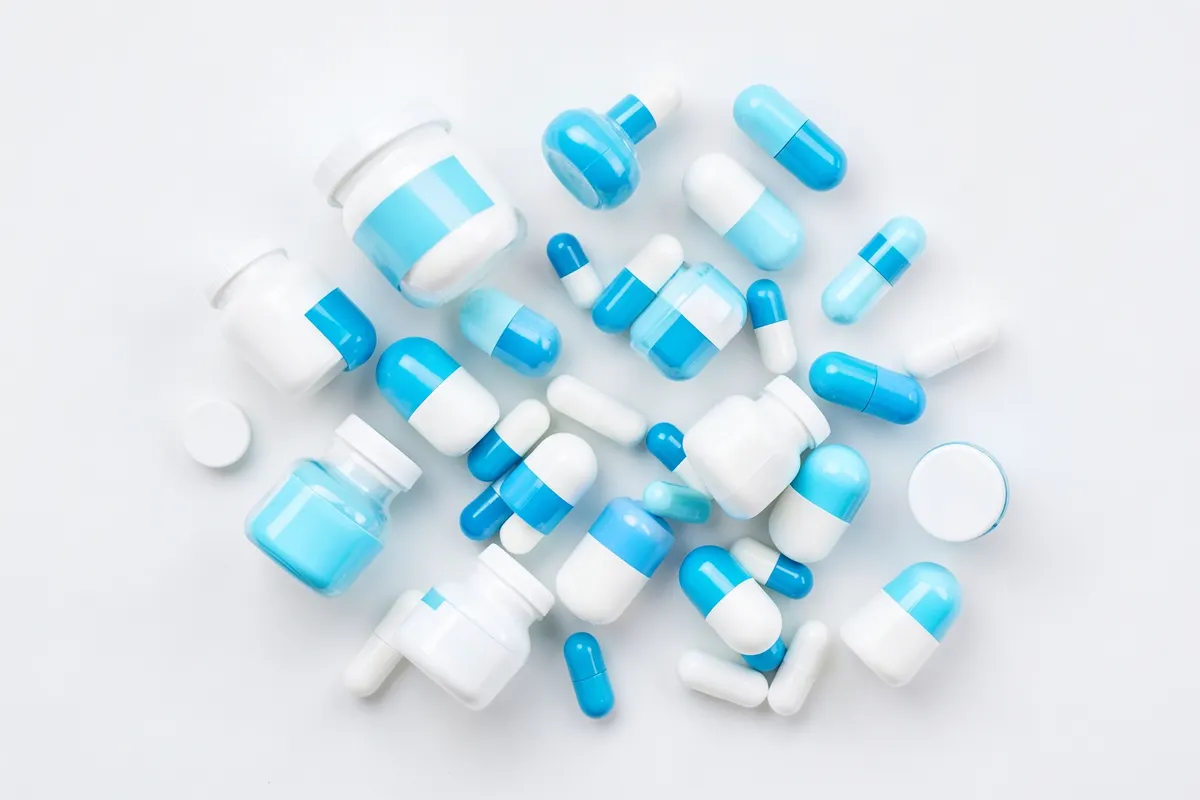 A collection of different sized pill bottles and capsules scattered on a white surface, representing pharmaceutical products and medication.