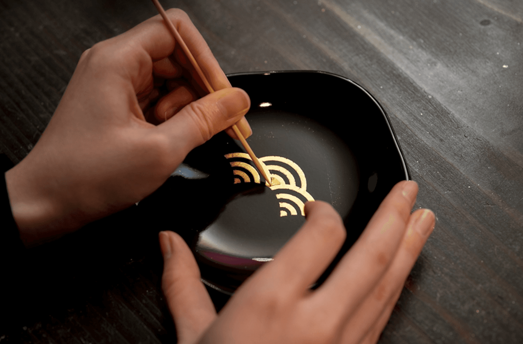 Artisan applying a gold decorative pattern by hand to black lacquerware.