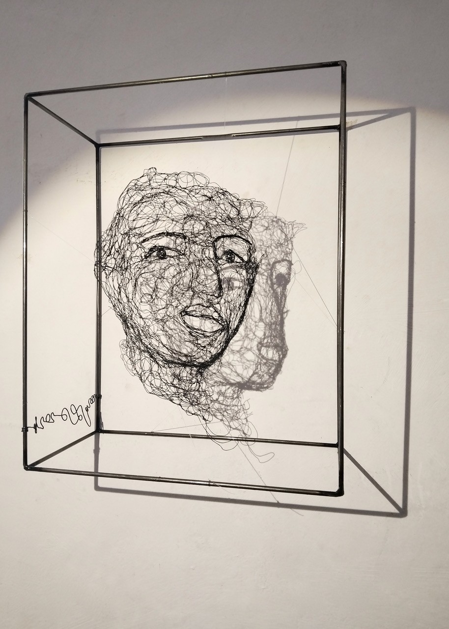 Sculpture en fil de fer représentant le visage d'une femme dans un cadre en fil de fer, vue détaillée de profil avec son ombre projetée sur le mur