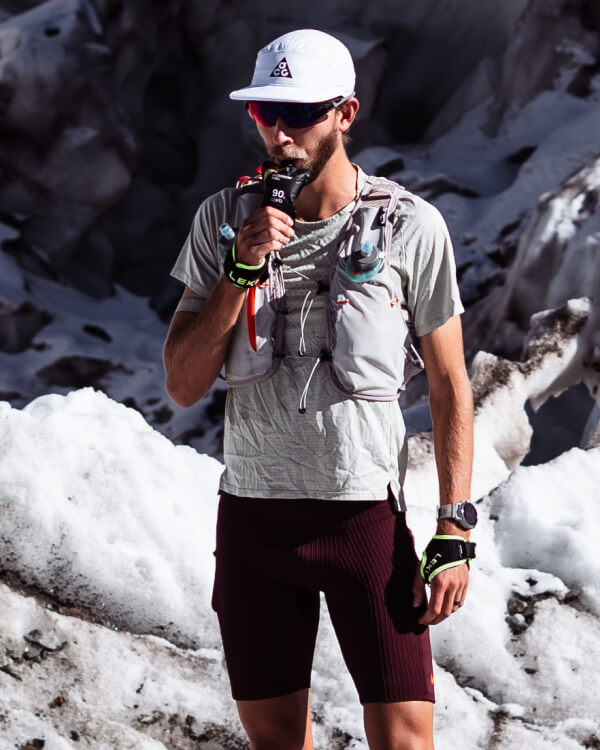 Caleb drinking from a bottle while standing on a snowy mountain trail.