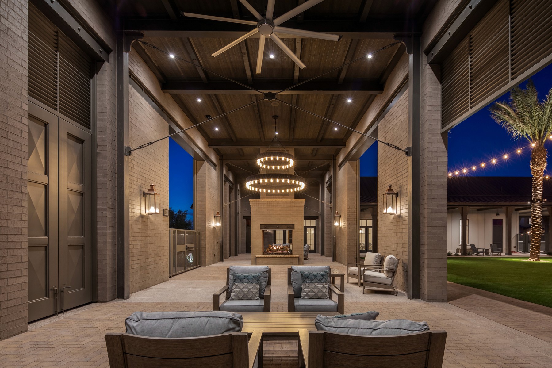 Outdoor patio with seating area, fireplace, and ceiling fan at night.  String lights are visible in the background.
