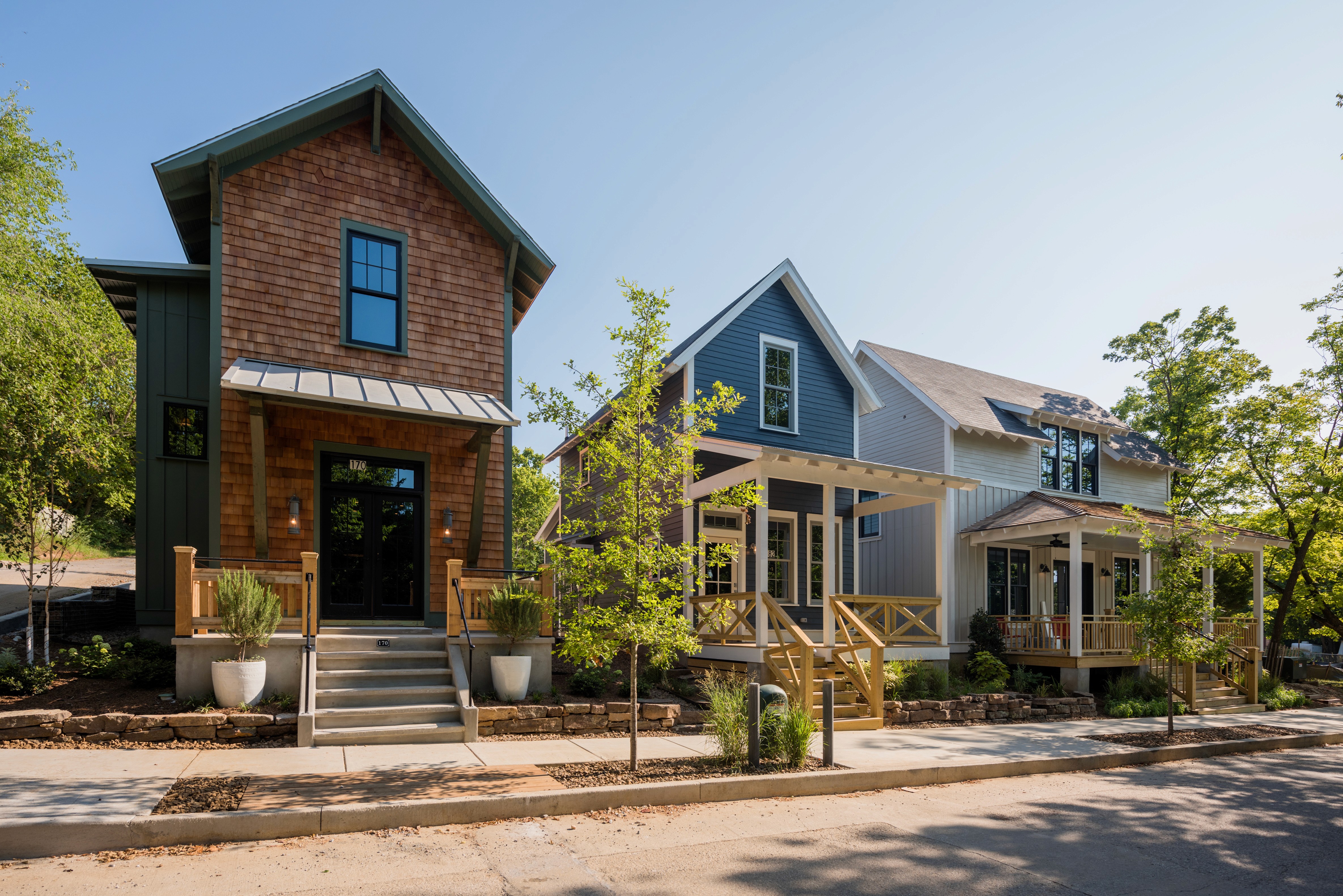 Three two story homes with front porches along a street with trees