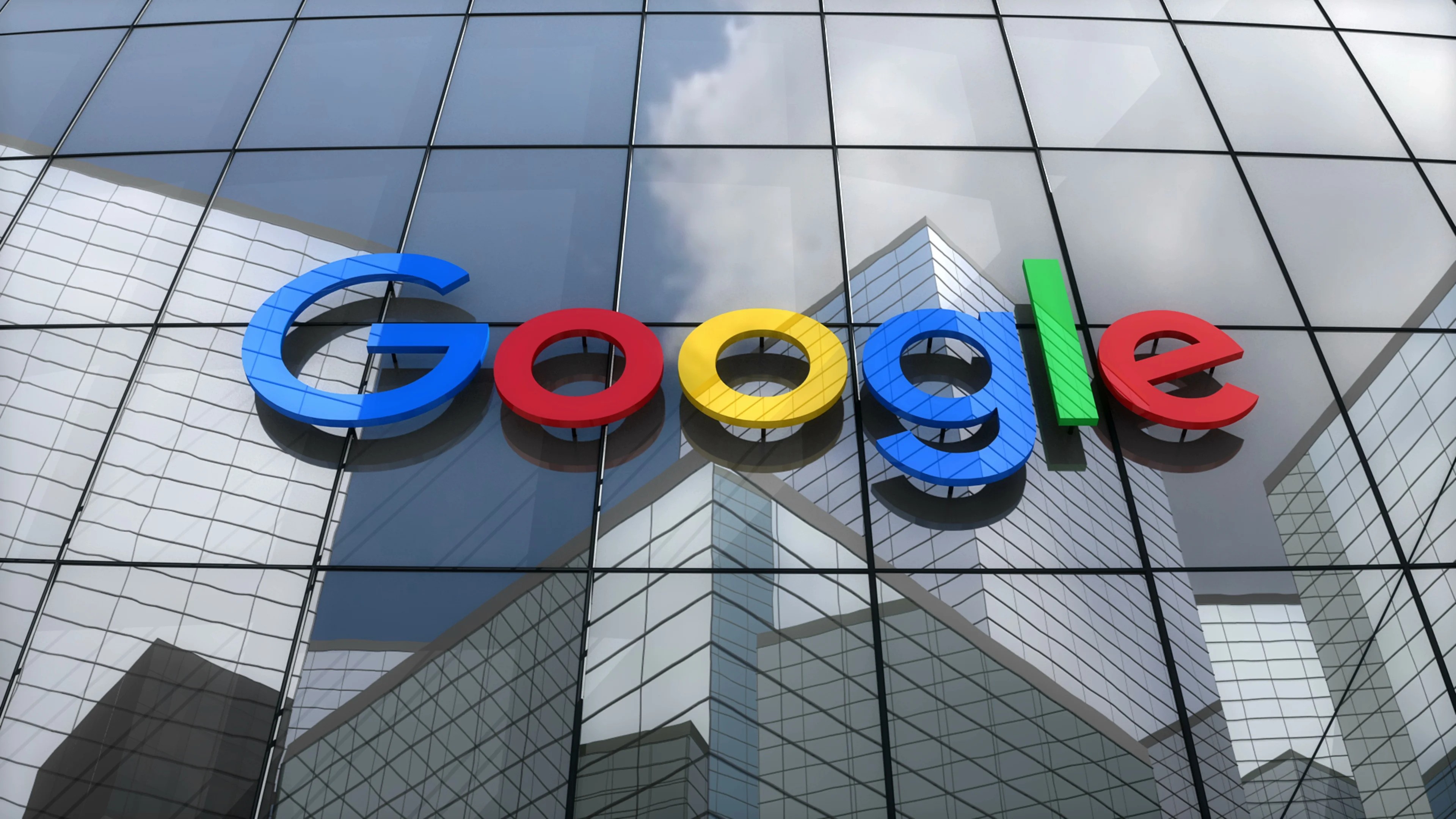 Google logo displayed in vibrant blue, red, yellow, and green on the glass facade of a modern building, reflecting the surrounding skyscrapers.