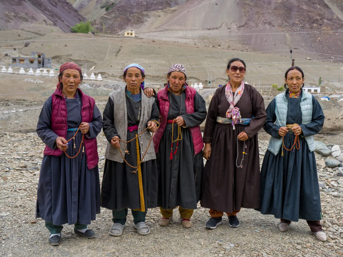 Cinco mujeres ladakhis con rosarios budistas frente a una hilera de estupas
