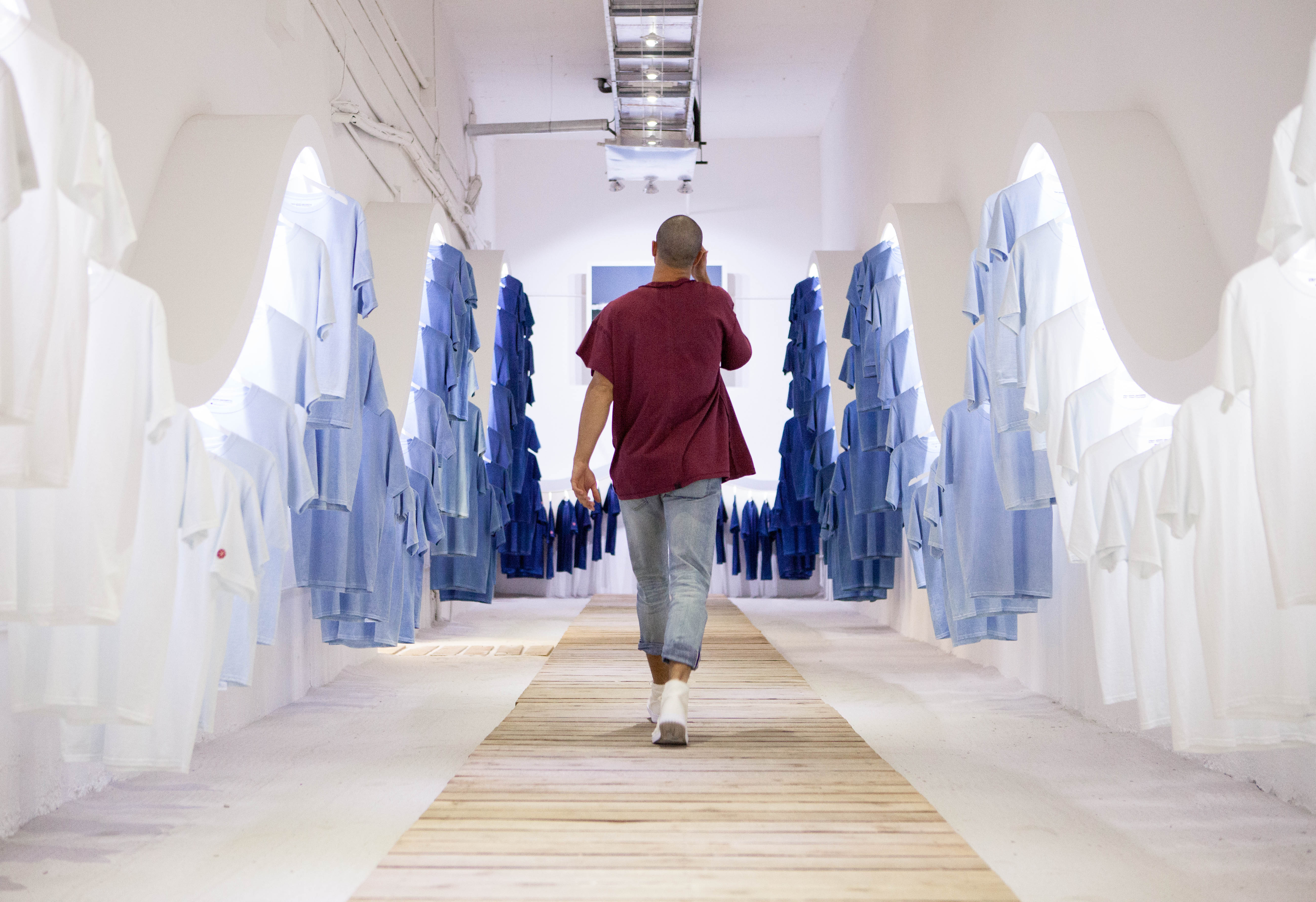 Person walking down a bright hallway lined with hanging garments during an New York Sunshine Art Basel installation.