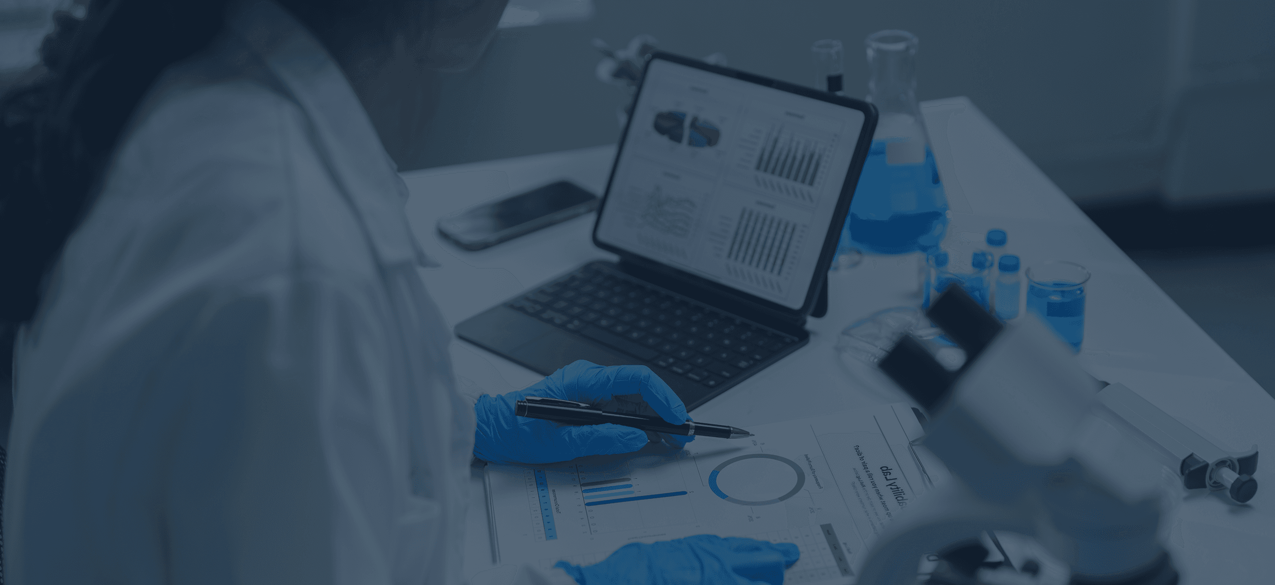 A scientist on a table with papers, laptop and laboratory equipment.