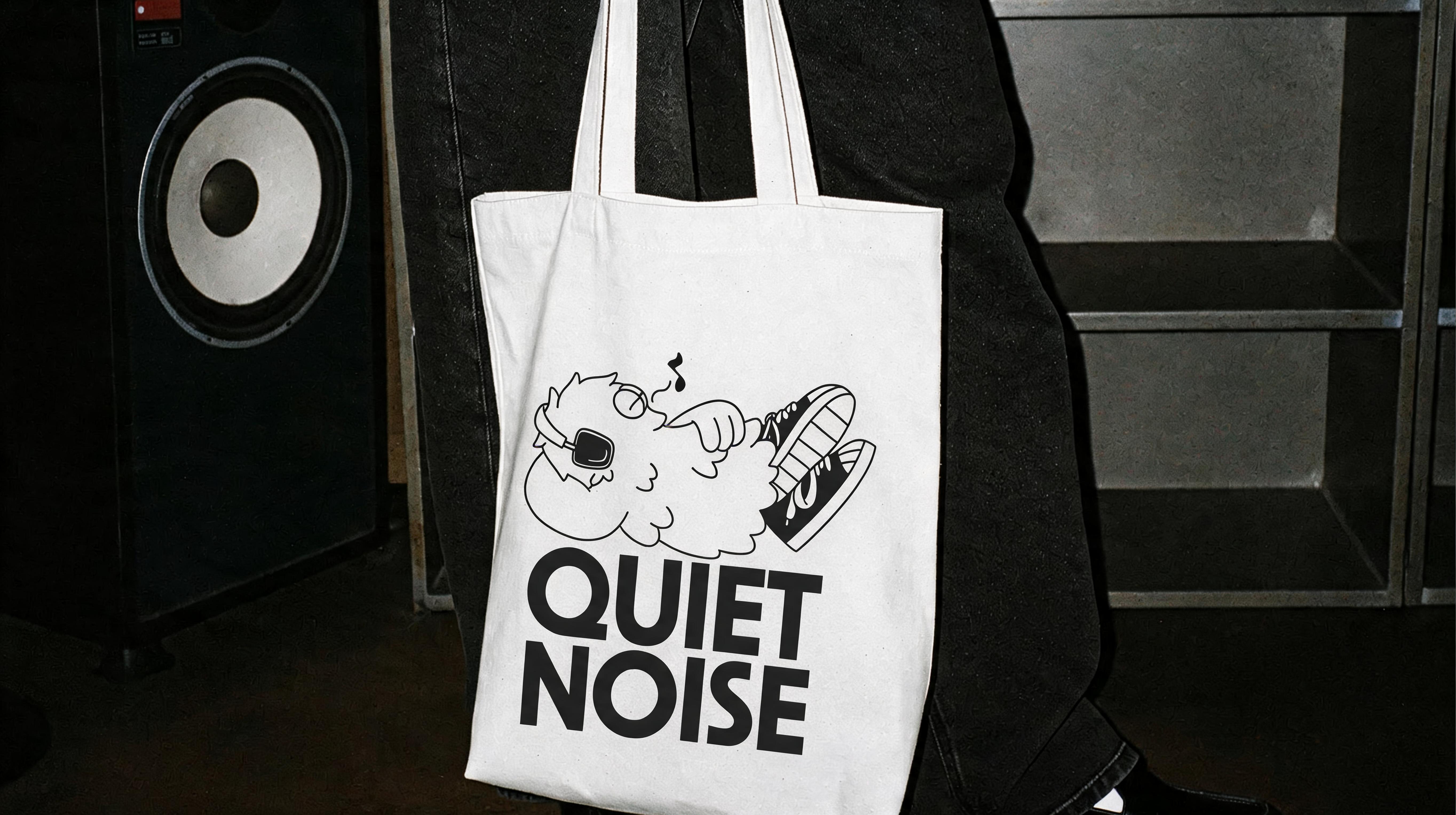 A white Quiet Noise tote bag with the mascot, carried past a speaker