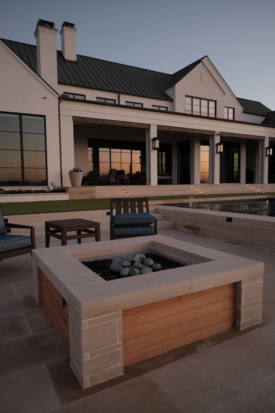 Custom built-in gas fire pit design at dusk with luxury pool and patio for Dallas Fort Worth property by Blount Designs