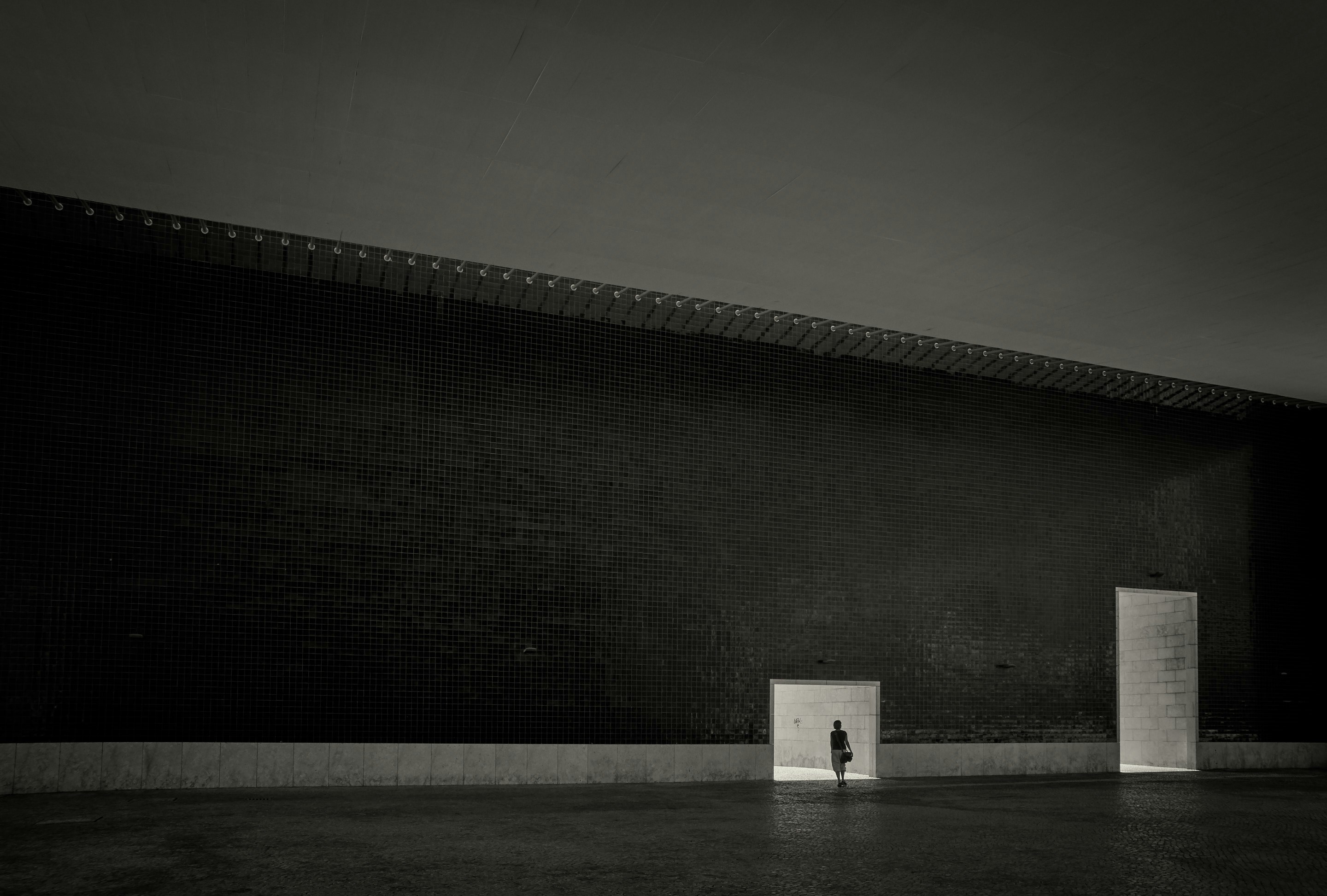 person standing in front of small tunnel beside of big tunnel grayscale photography