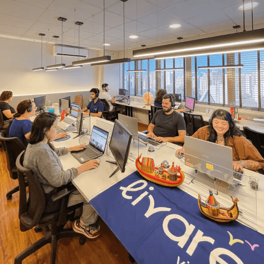 Equipe da Livare Viagens trabalhando em escritório moderno, com colaboradores em estações de trabalho e ambiente corporativo organizado