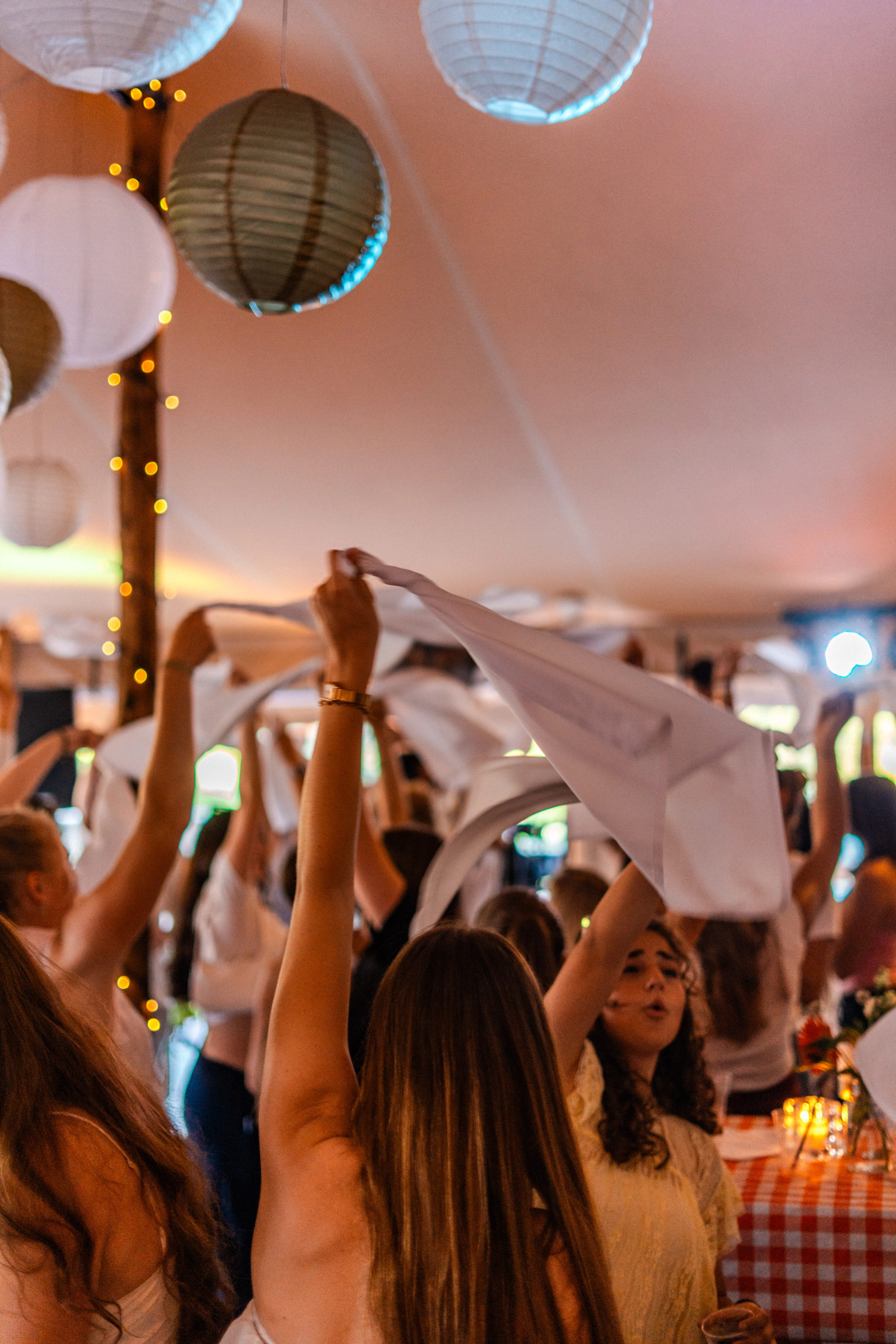 Gasten zwaaien met servetten onder lampionnen in de feesttent