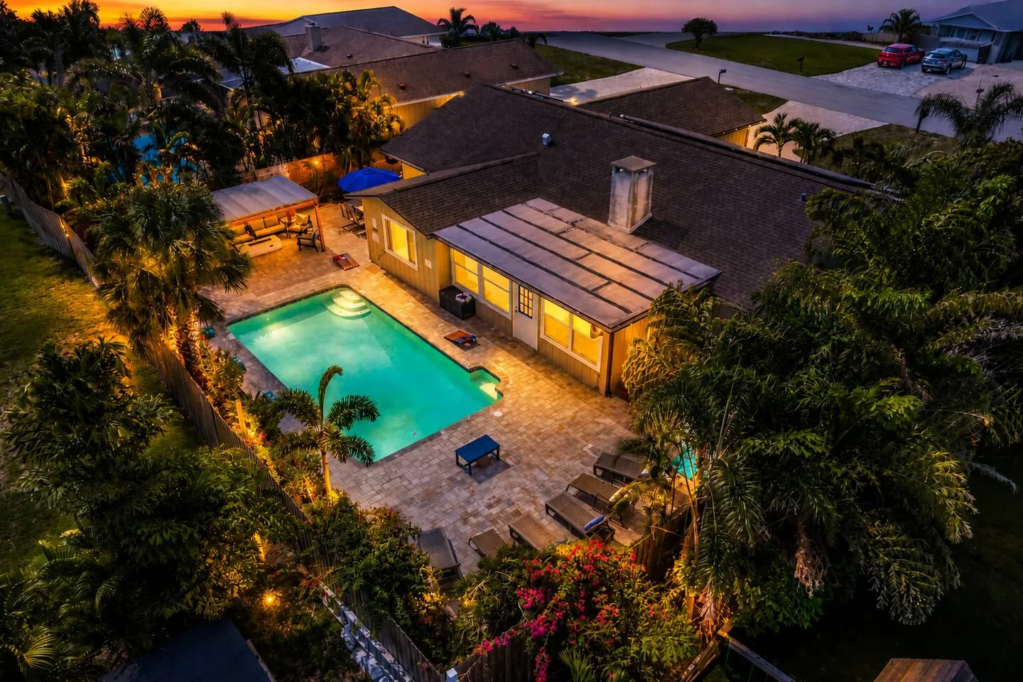 Aerial at dusk with house, lit pool and pergola, neighbors' cars visible at Sarasota Beach Bungalow, Bradenton, Florida