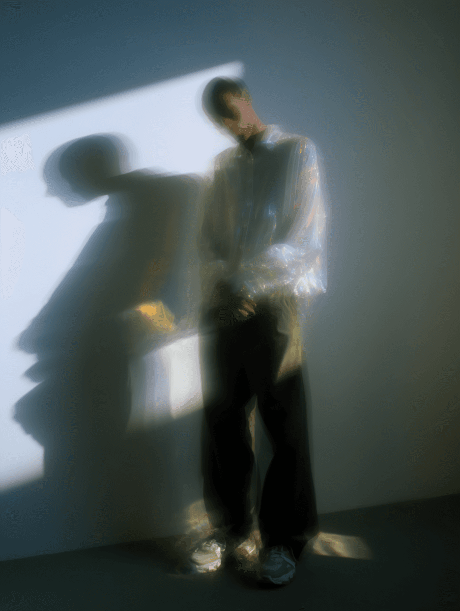 Blurred fashion portrait of a person wearing a reflective shirt, standing in soft light with motion blur and shadow