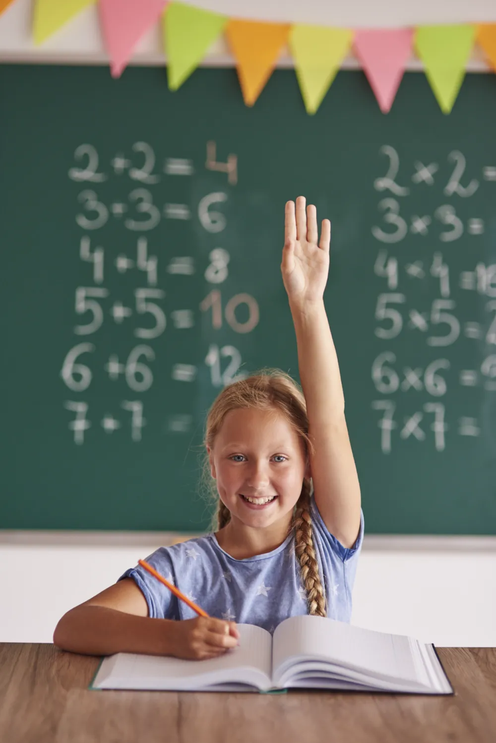 Girl holding hand up in front of blackboard with sums on 