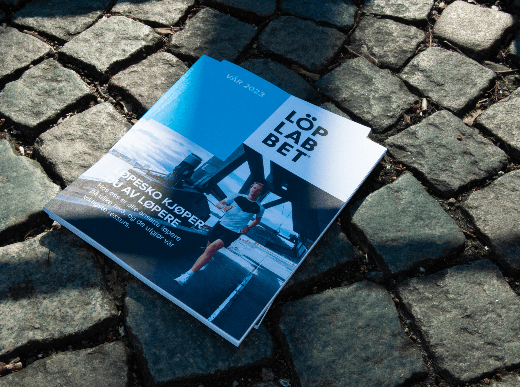 Two editions of Löplabbets spring magazine laying on the ground outside on cobblestone in the sunshine. 