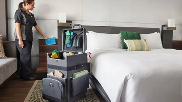 A housekeeper cleaning a hotel bedroom and uses a Rubbermaid Commercial Executive Quick Cart
